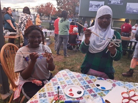 A pair of black girls, one in a head scarf the other not, making flowers from toilet paper rolls at a Manchester festival
