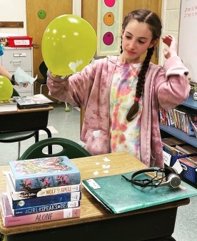 A girl picking up pieces of tissue paper with a static charge on her balloon