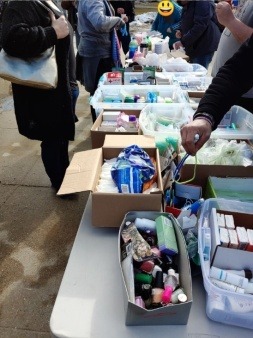 A folding table holding boxes of personal hygiene items with people standing on both sides.