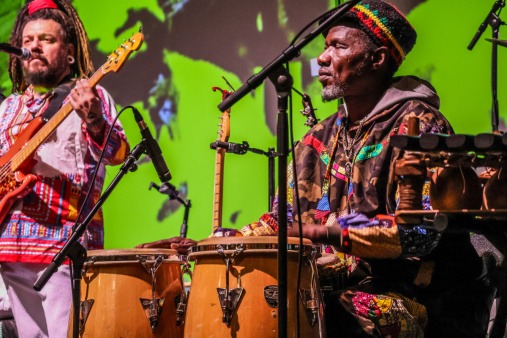 All the Rivers bassist, Mal Maiz, and All the Rivers percussionist Assane Coly during the Flynn benefit concert on March 11 All the Rivers bassist, Mal Maiz, pictured with All the Rivers percussionist Assane Coly, both wearing colorful, traditional clothing representing their culture on stage at the Flynn benefit concert