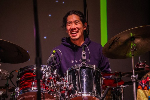 All the Rivers percussionist Daiki Hirano during a soundcheck for the All the Rivers benefit concert at the Flynn on March 11 All the Rivers percussionist Daiki Hirano smiling and playing the drums during an All the Rivers soundcheck on the Flynn stage