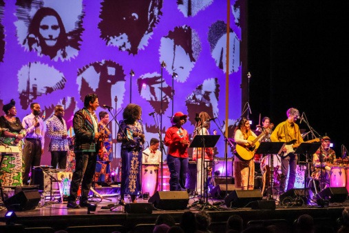 All the Rivers performing live at the sold-out Flynn benefit concert on March 11, 2026 All the Rivers performing live at the Flynn, wearing colorful clothing and performing before a vibrantly lit backdrop in purple hues