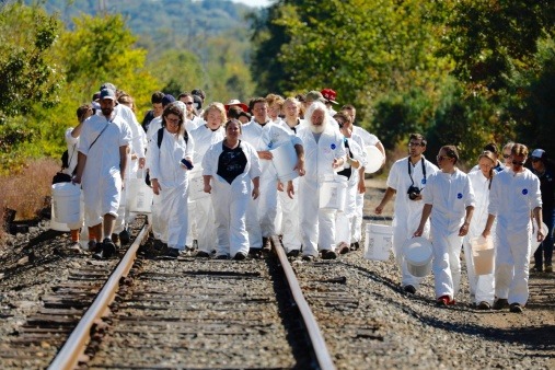 A group of protesters walking down railroad tracks wearing tyvek suits, carrying buckets and shovels and singing