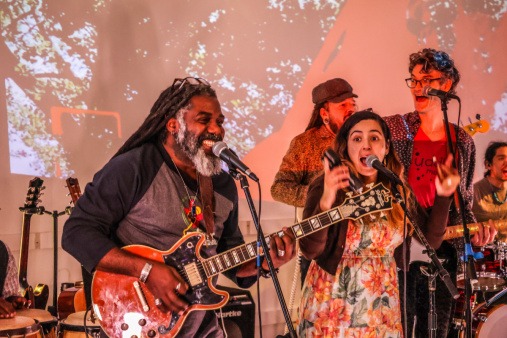 All the Rivers ensemble members Steeve Valcourt, Cintia Lovo, and director, Avi Salloway rehearsing before the Flynn benefit concert All the Rivers ensemble members Steeve Valcourt, Cintia Lovo, and Avi Salloway singing and smiling during an All the Rivers rehearsal