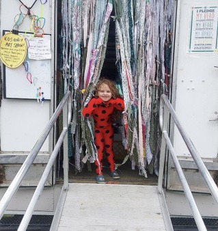A young fashionista poses at the opening of the Joy Truck in a red jumper looking through a hand-made curtain
