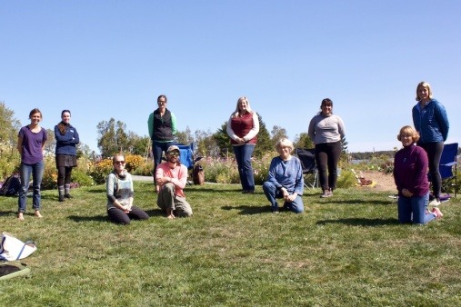 People 6 ft apart standing in a park smiling at the camera. 