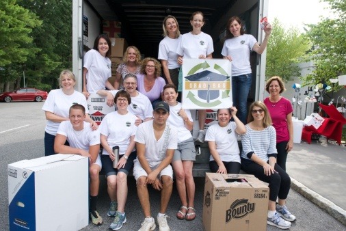 photo of a group of people sitting inside of and in front of an open moving truck. There are boxes of dorm items behind the group.