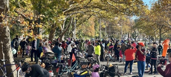 A large group of people, standing alongside a road full of parked bikes, with no cars. 