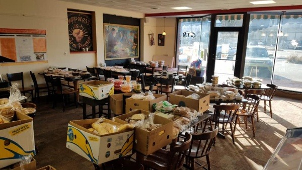 Dozens of boxes filled with food sit on tables and chairs, ready for distribution to community members