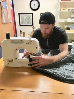 Man repairing sleeping bag with sewing machine.