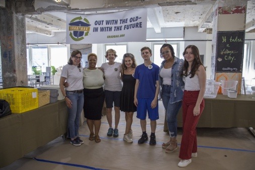 Group of Grad Bag staff and volunteers standing underneath a banner that reads "out with the old, in with the future"