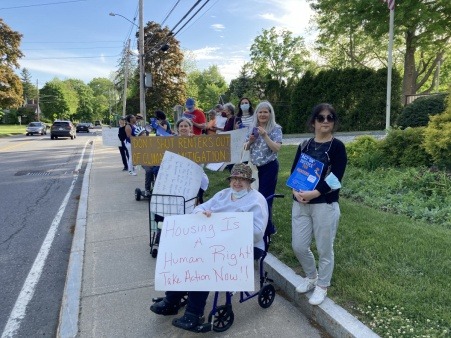 Members of Housing and Climate Justice for Acton marched to Town Hall in May 2022 and attended a Select Board meeting in order to get the Town to include housing stabilization services in its goals.  Several weeks later, the Select Board created a set of goals that include offering housing stabilization services..