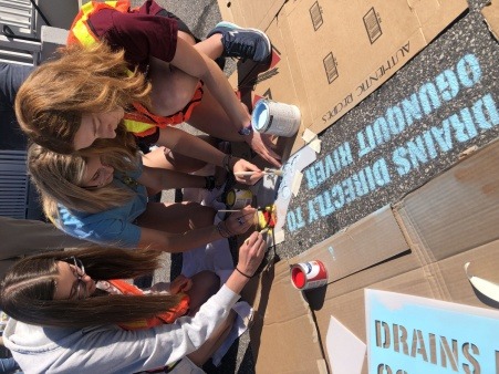 Student volunteers paint storm drains