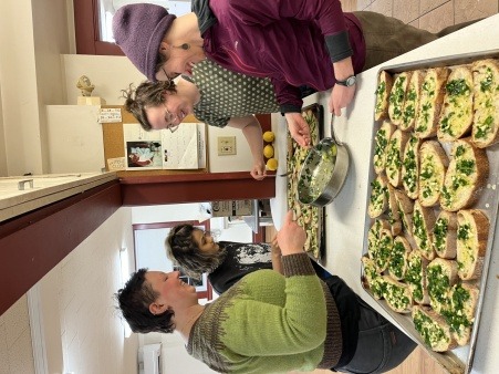 A group of four people stand at a counter applying garlic butter to slices of bread