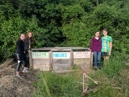 Four From The Ground UP leaders stand next to their community compost they built and maintain