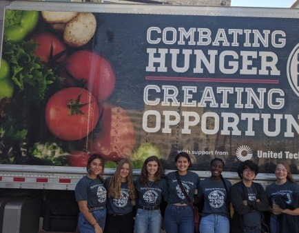 Seven From The Ground UP leaders standing in front of a sign "combat hunger. Creating opportunity"