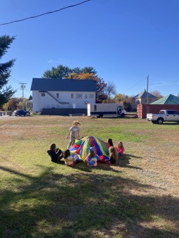 In front of the Joy Truck and field kids play in the sun with a parachute game, a favorite 4H movement activity.