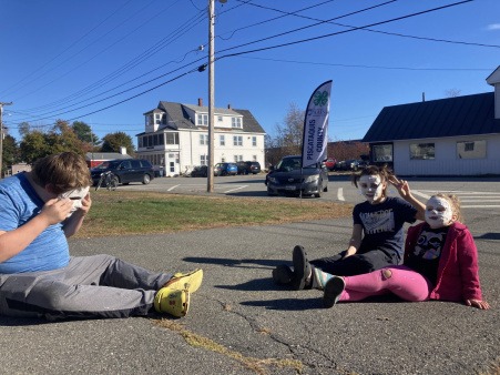 Three Joy Truck 4H kids sit in the sun drying their masks that were made collaboratively. In the distance the Pisctataquis County 4H flag.