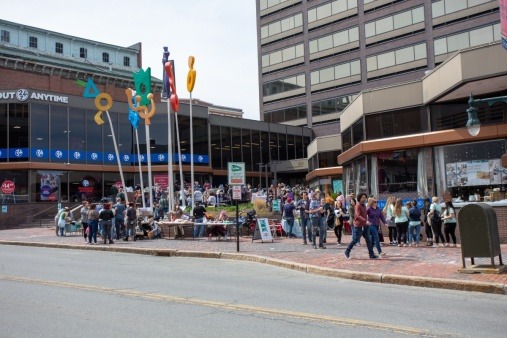 Image features a wide shot of the Ocean Gate courtyard on Congress St, full of queer artists and community members shopping local