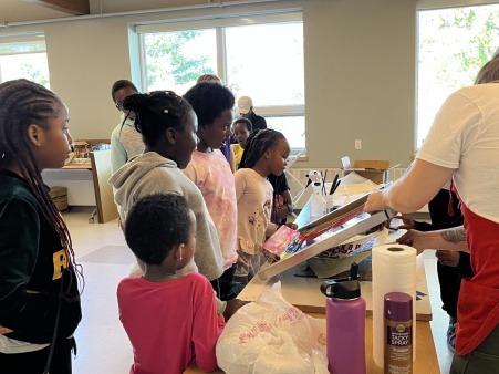 photo of youth from Project STORY with joyful expressions and open mouths as they watch a screenprinting demonstration before their chance to print