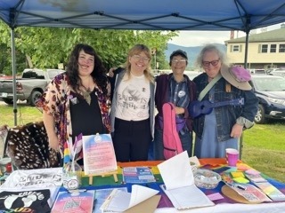 Three people stand behind a table of brightly colored materials at a pride event in North Conway, NH