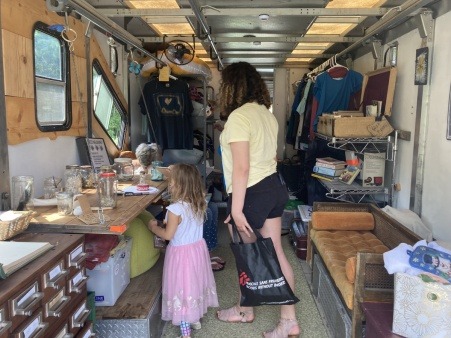 A grandmother sits inside the truck while a teen visitor and her young sister examine the Nature Library Guessing Game. 