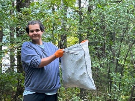 Chair of the Board of Directors holding a full trash bag in the woods.