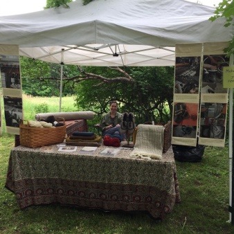 a woman sits under a tent with locally produced woolen yarns and cloth and 