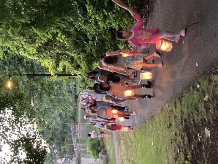 People carry lit bottle lanterns into the shadow of the trees.