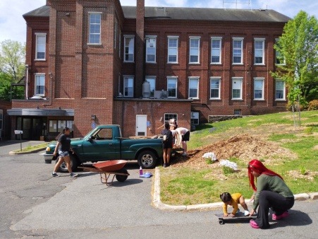 Group member showing her toddler how to use a skateboard during a work day at Montague Town Hall