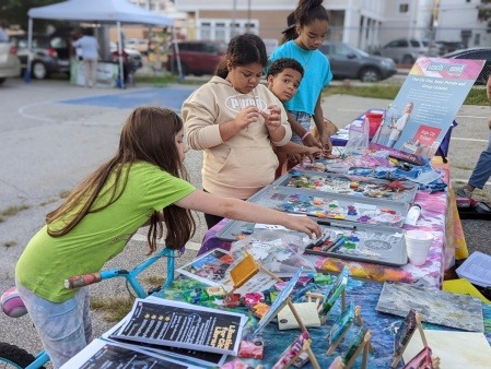 a group of children lined up at a table outside full of fun art supplies and lots of blue