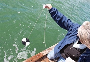 A volunteer holds a black and white secchi disk used to measure water clarity