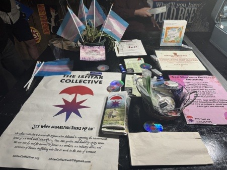 a table of harm reduction materials, plants, and pride flags next to some resource lists and current events