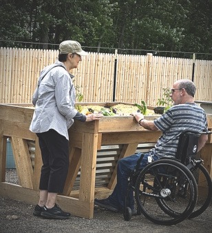 Two friends plant one of BCG’s wheelchair-accessible raised beds, designed so people with different mobility needs can garden, contribute, and belong together. Wheelchair-Accessible Garden Bed