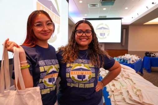 photo of two Grad Bag volunteers assisting at a Giveaway Day Event; standing in front of a table of donated items